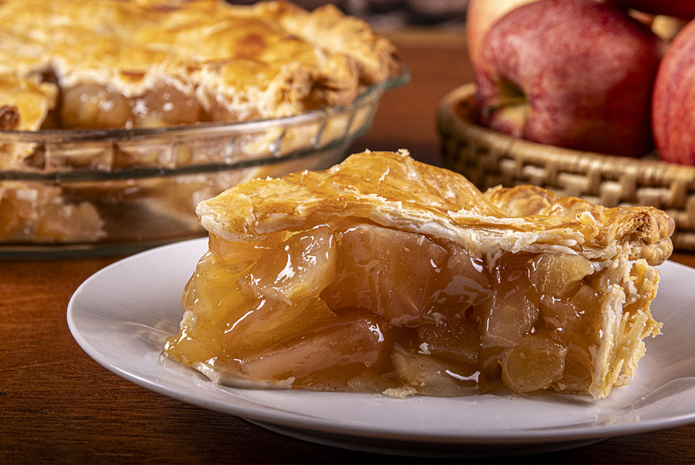 apple pie in a dish with a piece on a plate in the foreground